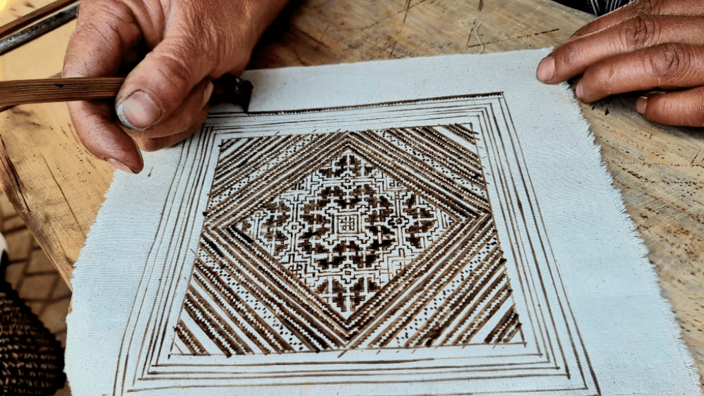 Artisan drawing freehand patterns on fabric with molten beeswax